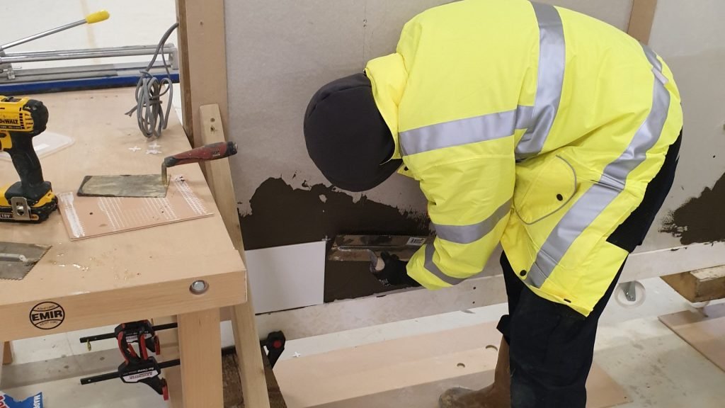 Male construction student tiling a wall