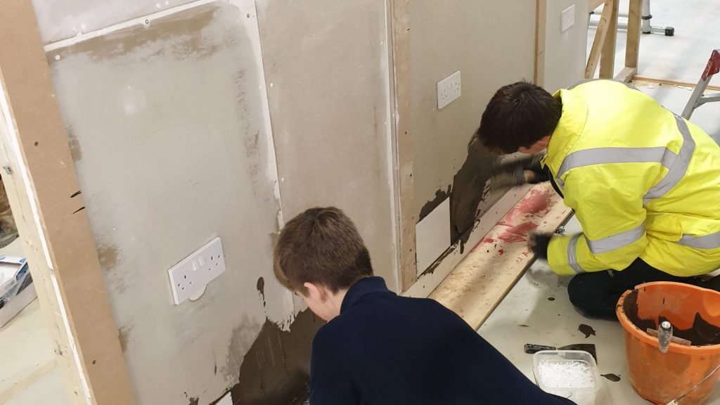 Male construction students tiling a wall