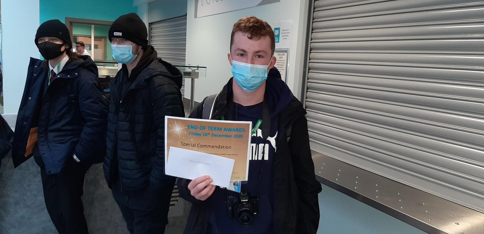 Male student in mask holding certificate