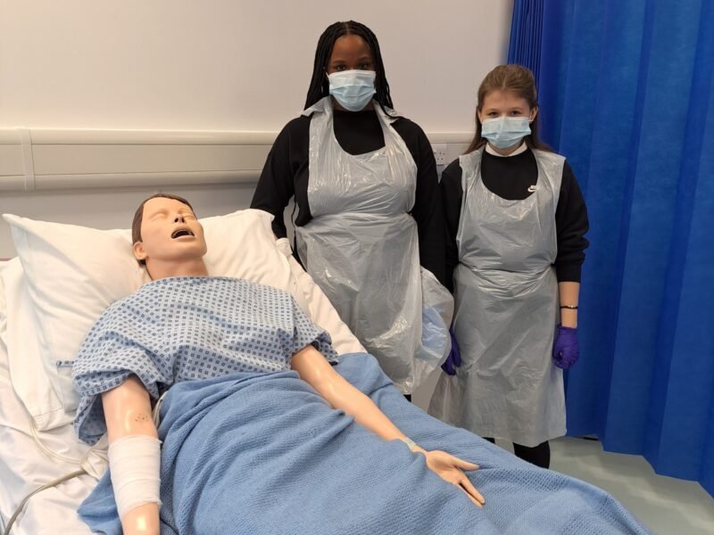 HSC studetns in masks and aprons next to dummy in hospital bed. learning environment at AUTC